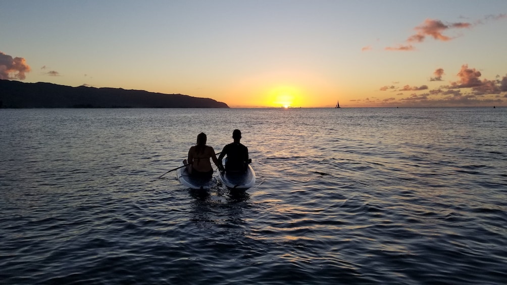 Couple enjoying views of the sunset while paddle boarding in Haleiwa