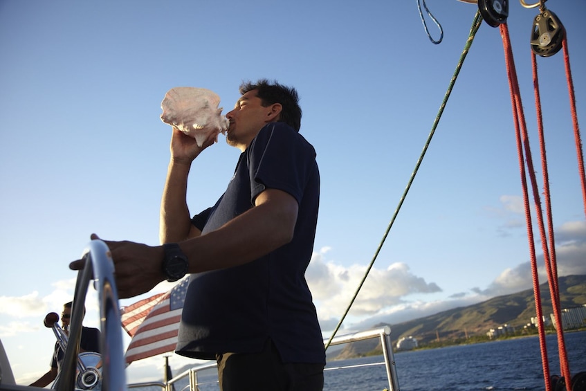 Man blows a horn aboard The Spirit of Aloha, a 54-foot sailing catamaran along the Waikoloa Coast 