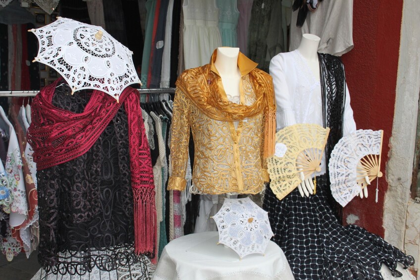 Boutique window view of clothing, fans, and scarves sold in Burano
