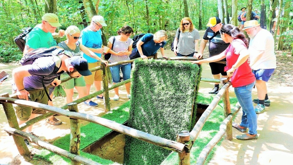 Tourists examine large trap door at Cu Chi Tunnels