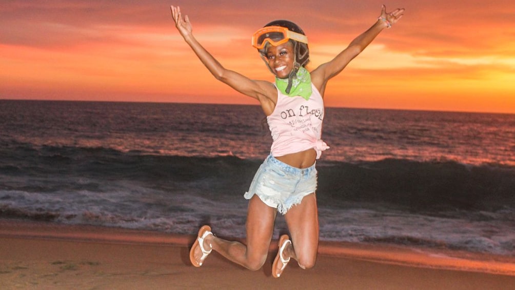 Woman with a helmet on jumps on a beach at sunset