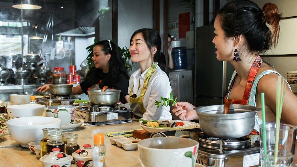 People sit around kitchen island with burners, pots, and ingredients at their work stations