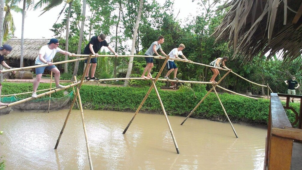 People walking across a bamboo bridge over a river in Vietnam