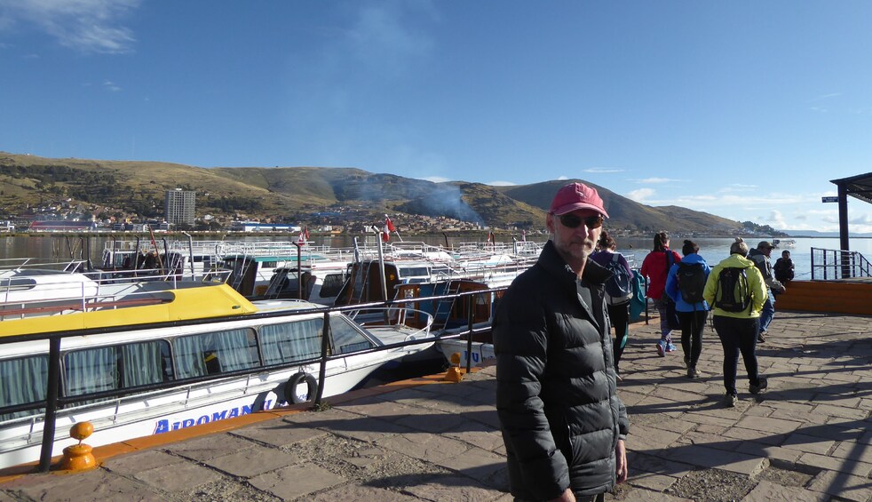 Man poses in front of boats docked near Lake Titicaca in Peru