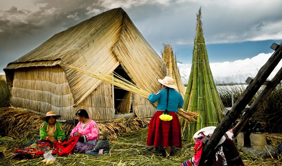Three Uros women work in front of entirely thatched house in Peru