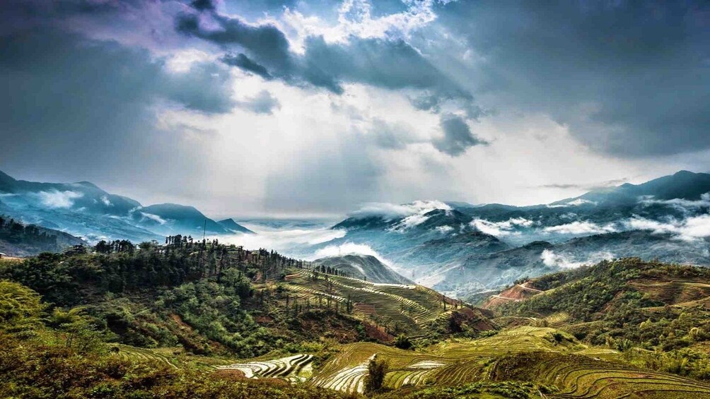 Sun shines through clouds onto mountains and fields of Sa Pa Valley, Vietnam