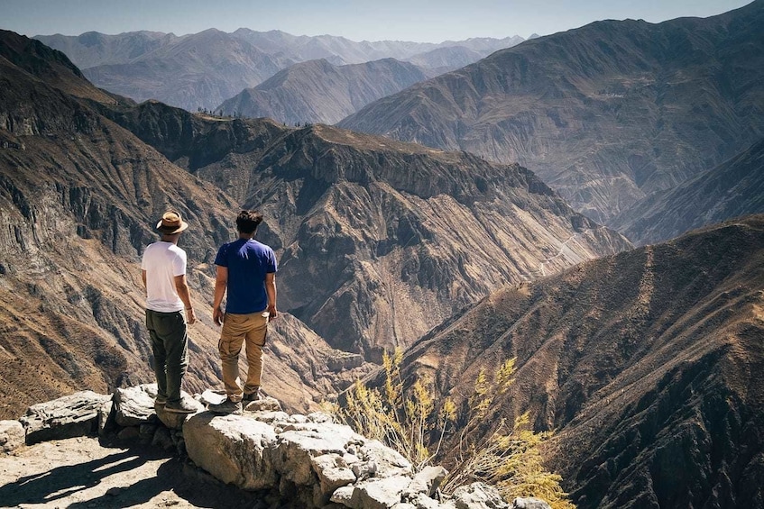 Two men stand on rocks overlooking Colca Canyon in Peru