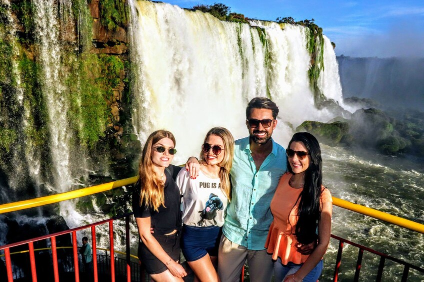 Tourists pose in front of Iguazu Falls on a sunny day