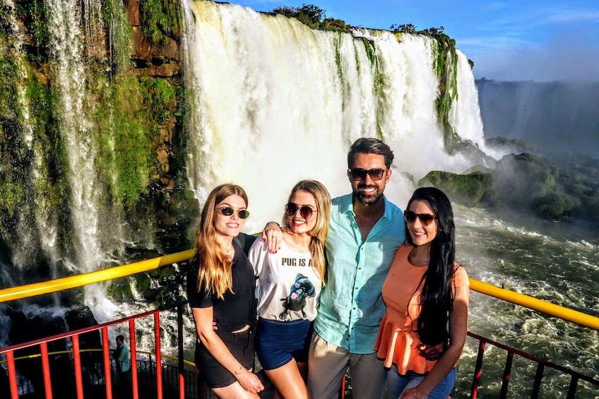 Tourists pose in front of Iguazu Falls on a sunny day