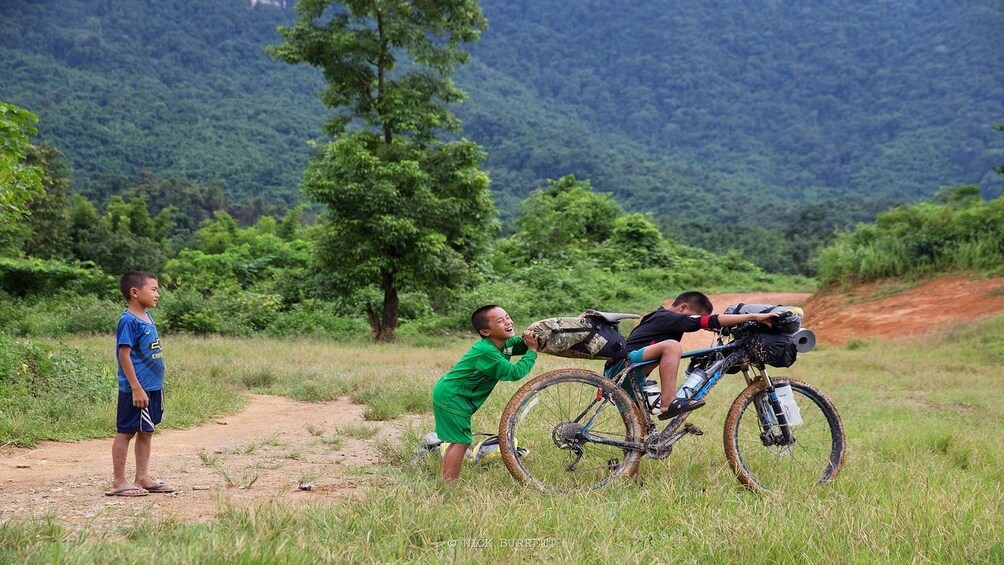 Lao children play on adult bike in field