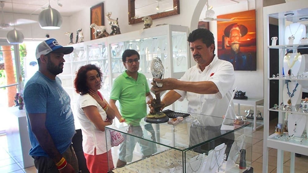 Shop owner shows tourists metal owl statue in Cabo San Lucas