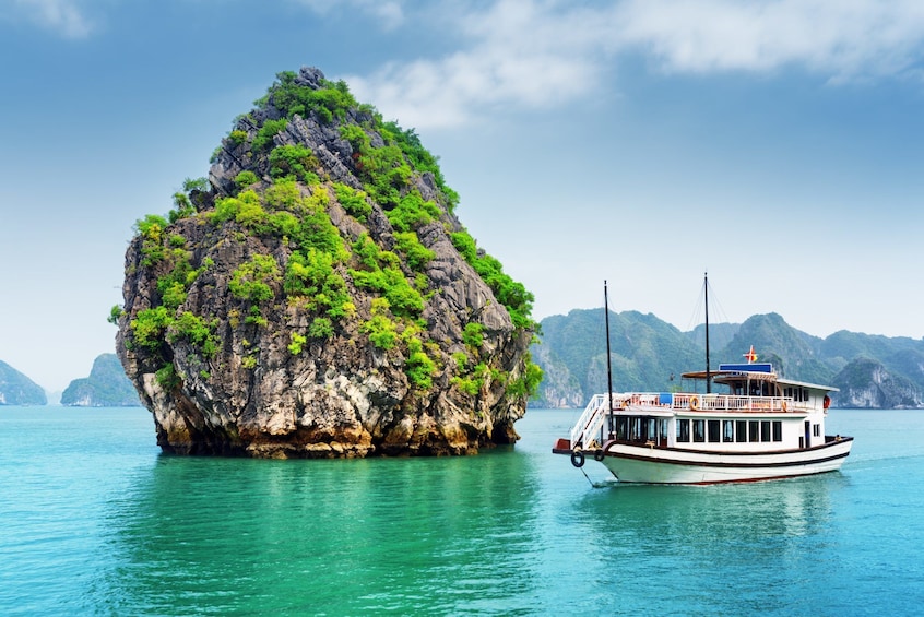 Boat near tall rock formation in Halong Bay