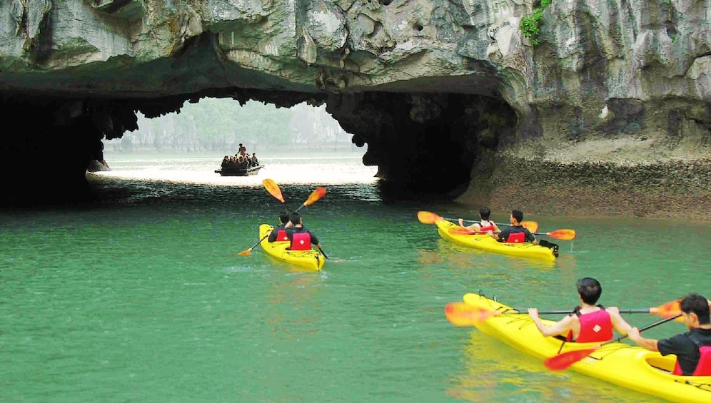 Tourists kayak under low opening in Halong Bay, Vietnam