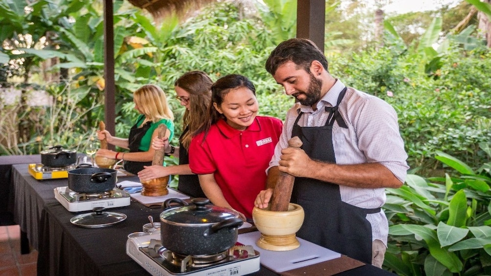 Man in apron muddles ingredients while instructor looks on