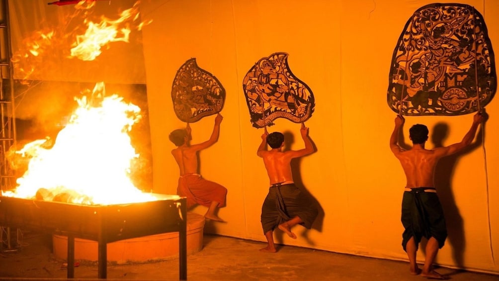 Show item 5 of 10. Three men hold up large fans against wall with fire behind them
