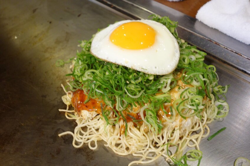 An egg on vegetables and noodles on a grill