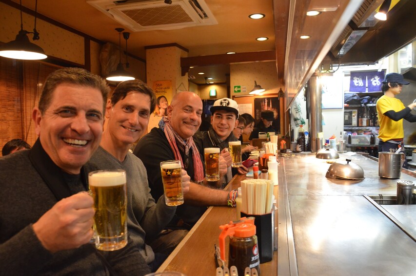 Group of men hold pints of beer at a bar top in Japan