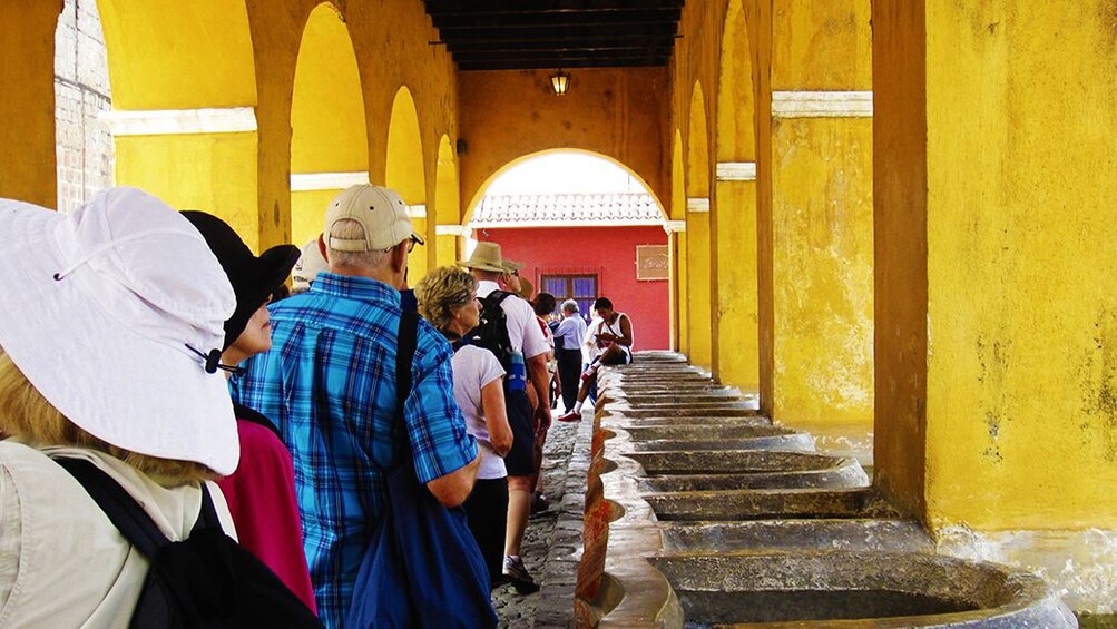 Tourists walk through bright yellow corridor of bathhouse in Antigua, Guatemala