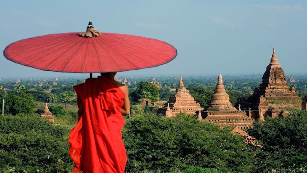 Monk holding a red umbrella while looking out at the temples in Myanmar