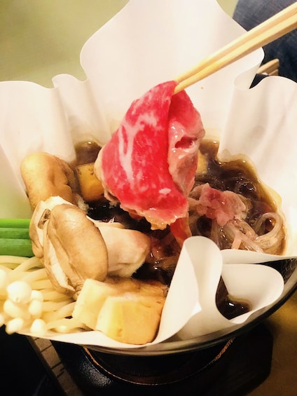 Chopsticks holding meat in a bowl of Japanese food