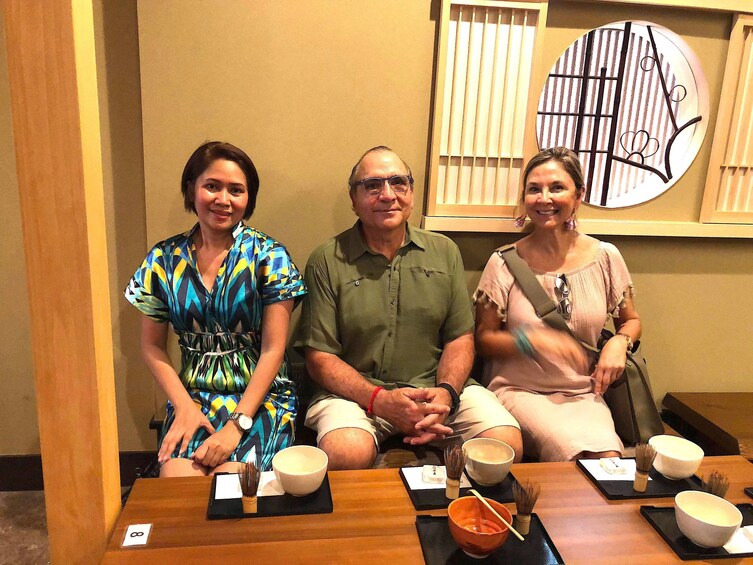 Three people sit at a table drinking tea