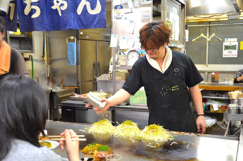 Show item 3 of 8. Person operates a grill at a market in Osaka