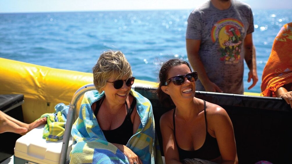 Two woman smile in bath suits and towels on boat