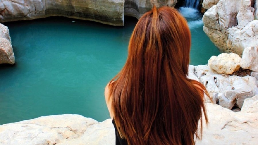 From behind, a woman looks over the clear pools at Wadi Ash