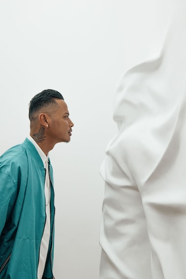 Man stares at sculpture of man stuck behind a white wall