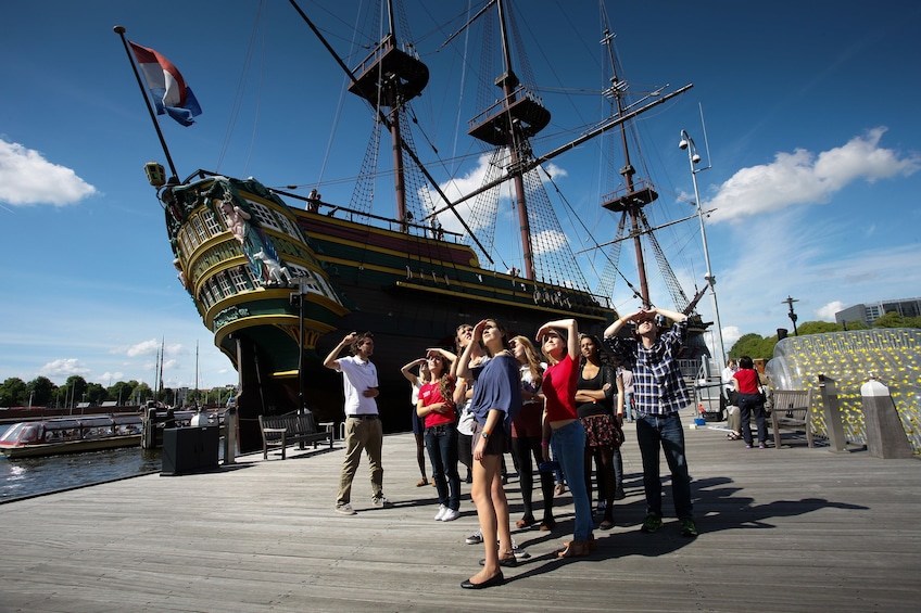 Tourists stand near The National Maritime Museum with a large ship behind them