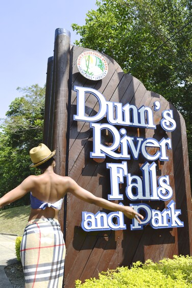 Woman standing next to sign for Dunn's River Falls and Park in Jamaica