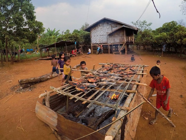 Small children watch fish cook over a fire in village in Laos