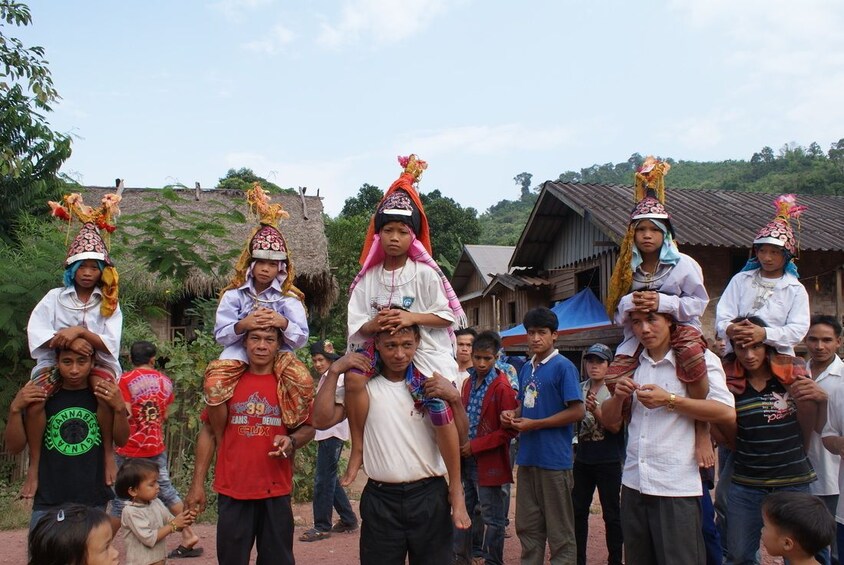 Children sit on men's shoulders in village in Luang Nam Tha Valley