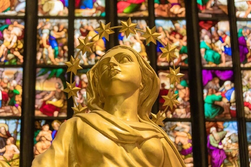 Colorful stained glass of the apse with the golden statue of the Madonna in the foreground at the Duomo Cathedral in Milan, Italy 
