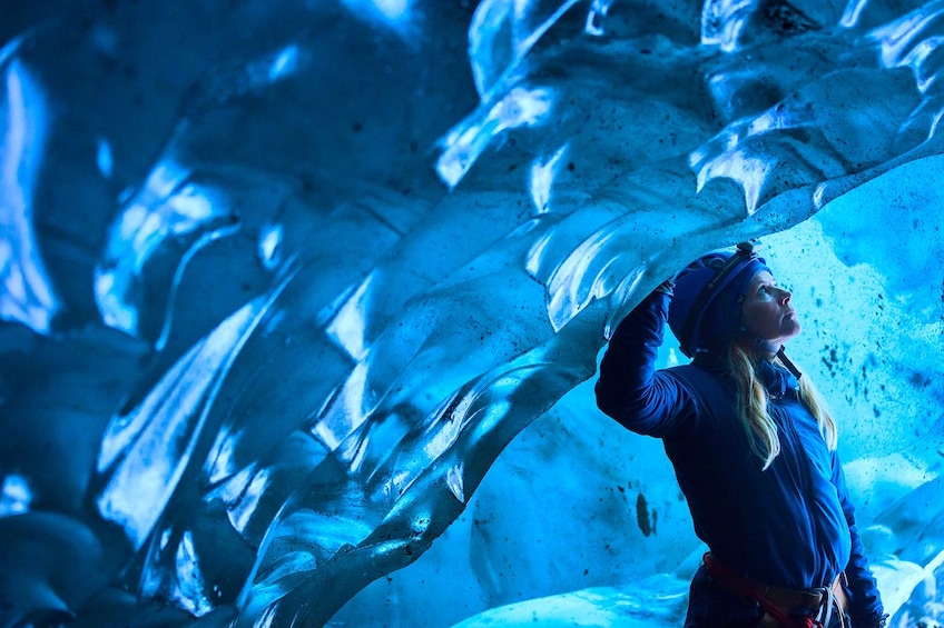 Woman with helmet stands near large ice wall in ice cave Skaftafell Glacier hike