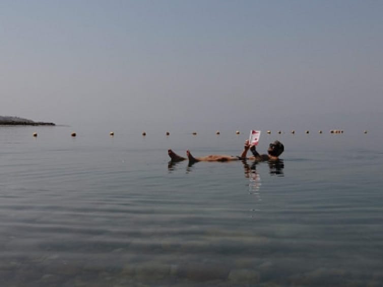 Man floating on the Dead Sea while reading a book 