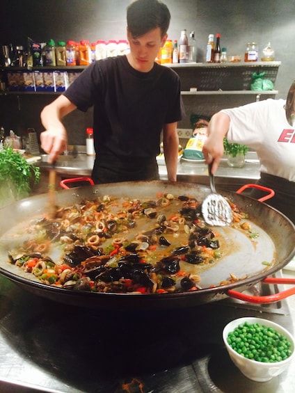 Man stirs large skillet of paella in kitchen