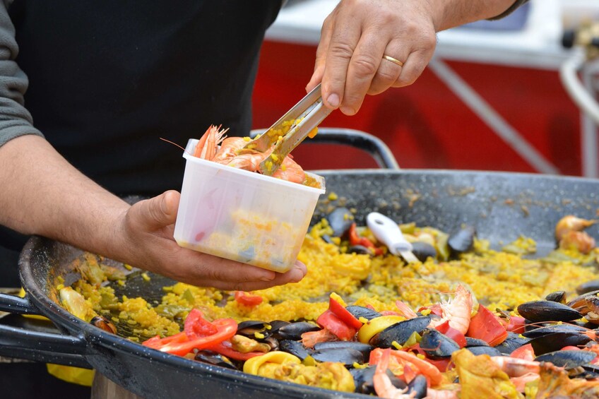 Man adds shrimp to large paella skillet