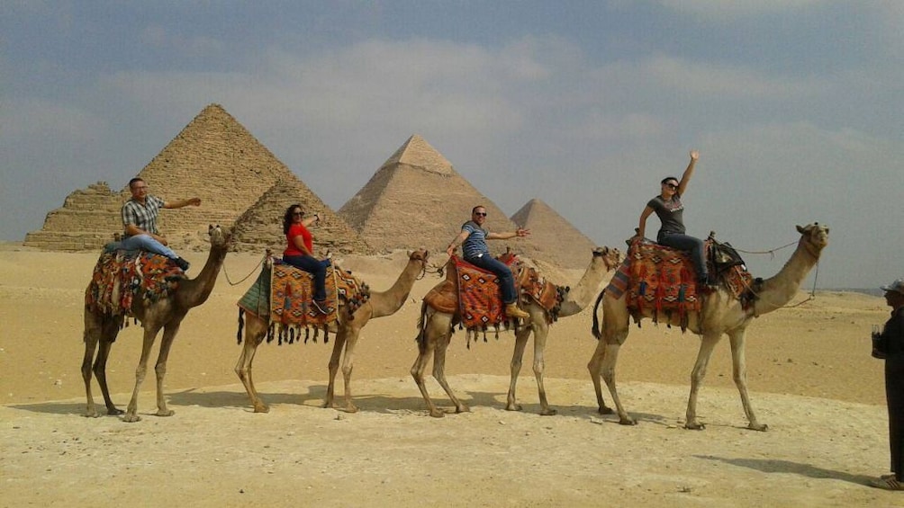 Line of people riding camels in front of Pyramids of Giza