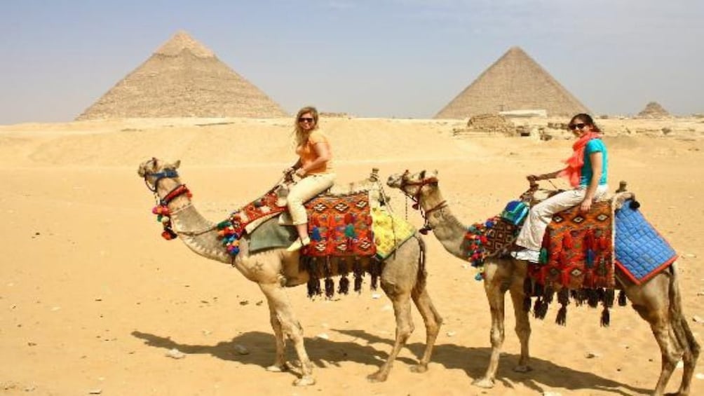 Tourists ride camels past the Pyramids of Giza