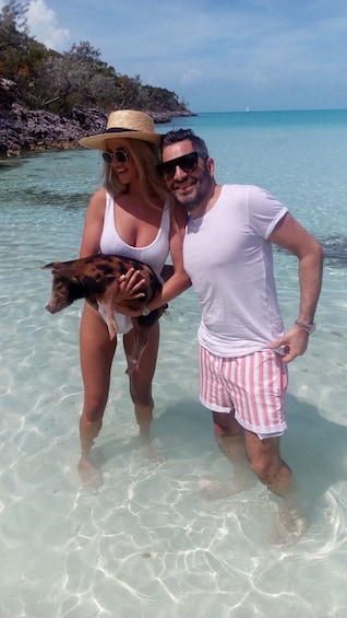 Man and woman hold pig in waters of Pig Beach