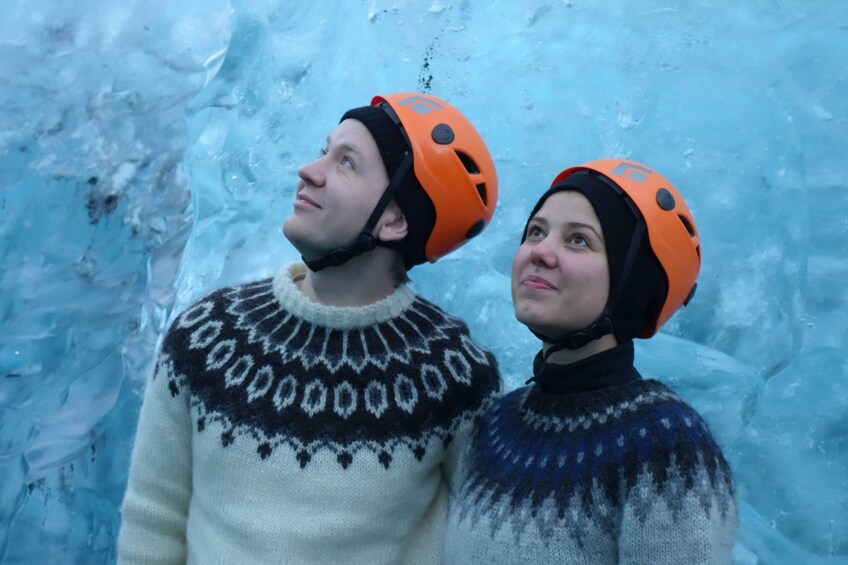 Two tourists with orange helmets in front of wall of ice