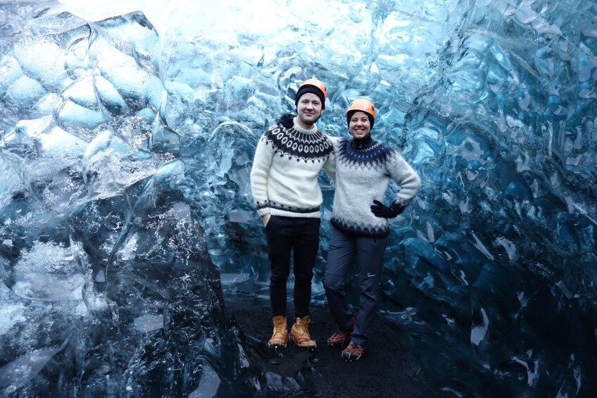 Two tourists with helmets pose in front of wall of ice