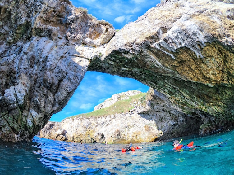 Snorkelers in water below stone arch