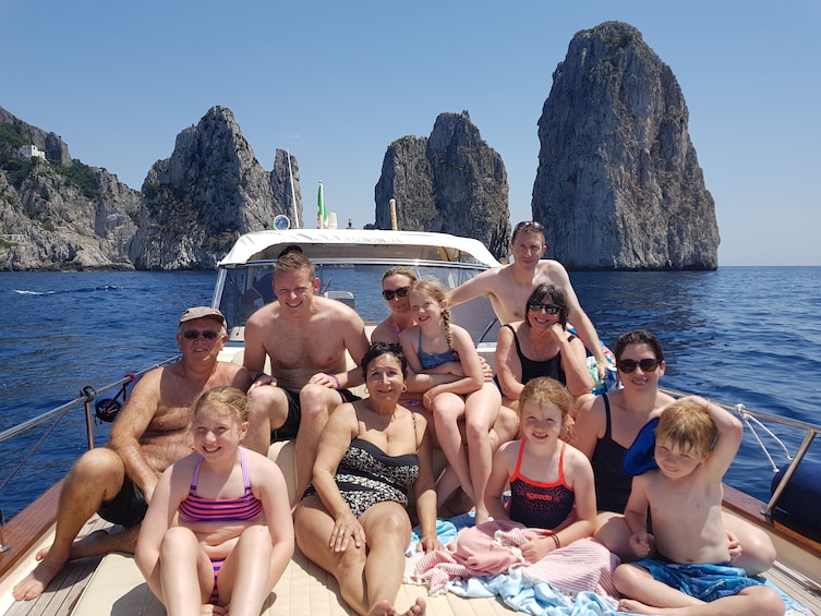 Show item 1 of 10. Large group of tourists pose on boat in front of islands of Capri, Italy