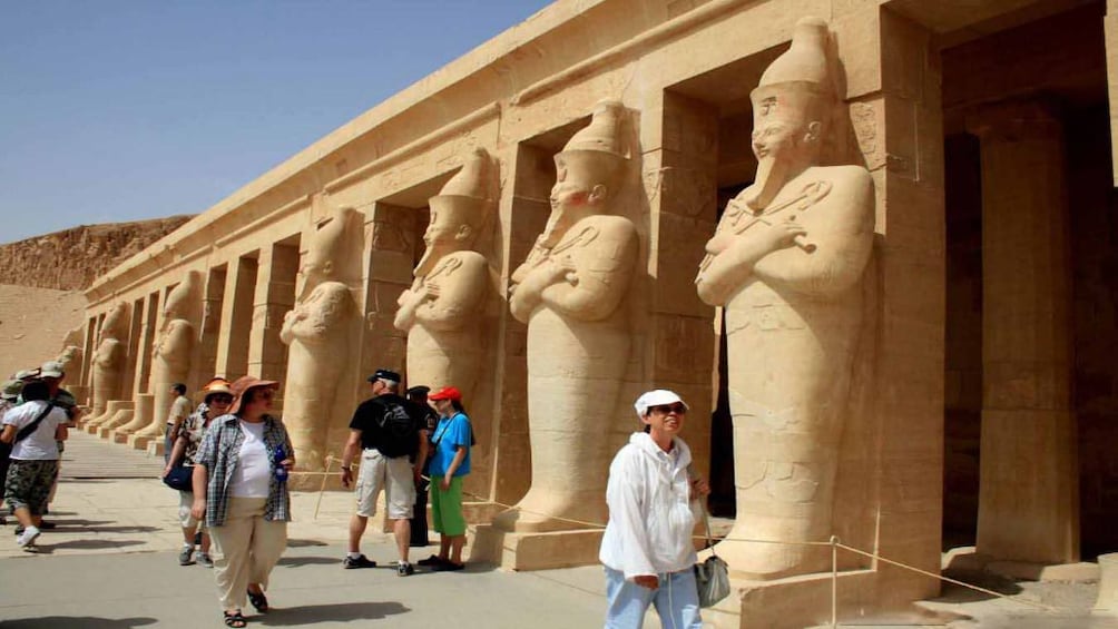 Tourists walk past large statues at entrances of Luxor Temple