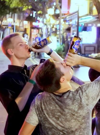 Two men drinking Tiger beers on the streets in Singapore at night 