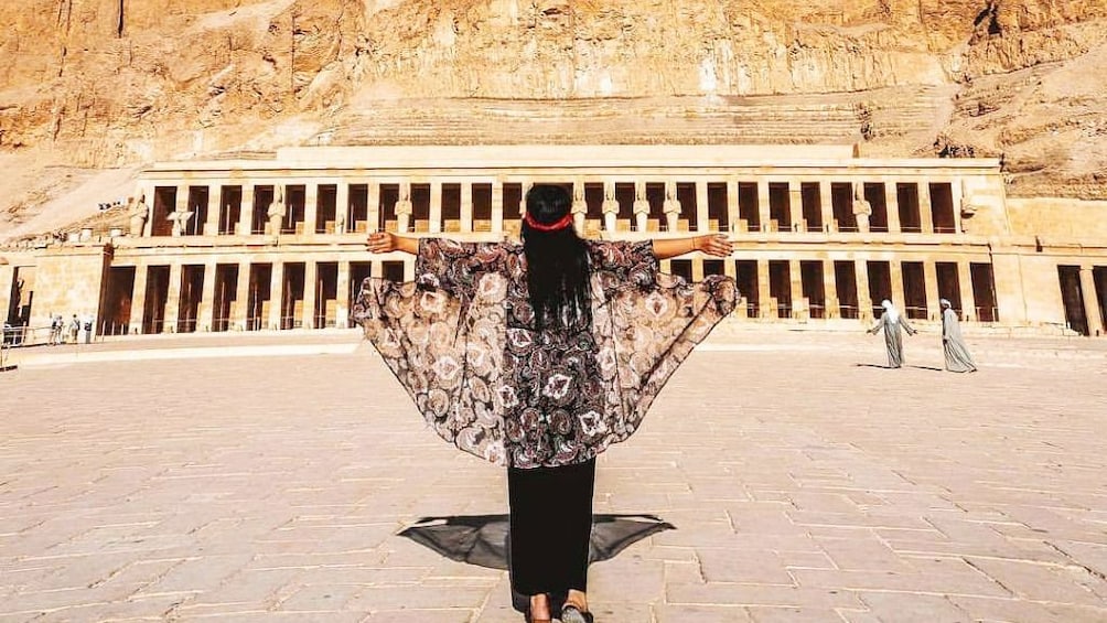 Woman poses with arms to her sides in front of Mortuary Temple of Hatshepsut