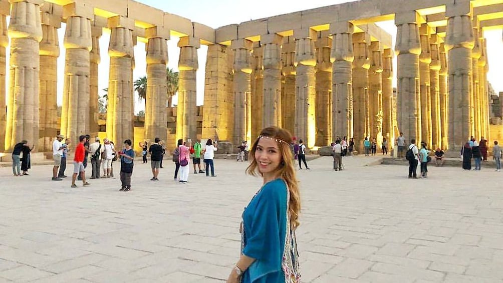 Woman stands on Egyptian plaza with columns in background 