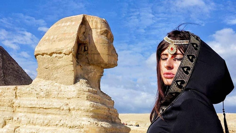 Closeup of woman's face next to head of large sphinx statue